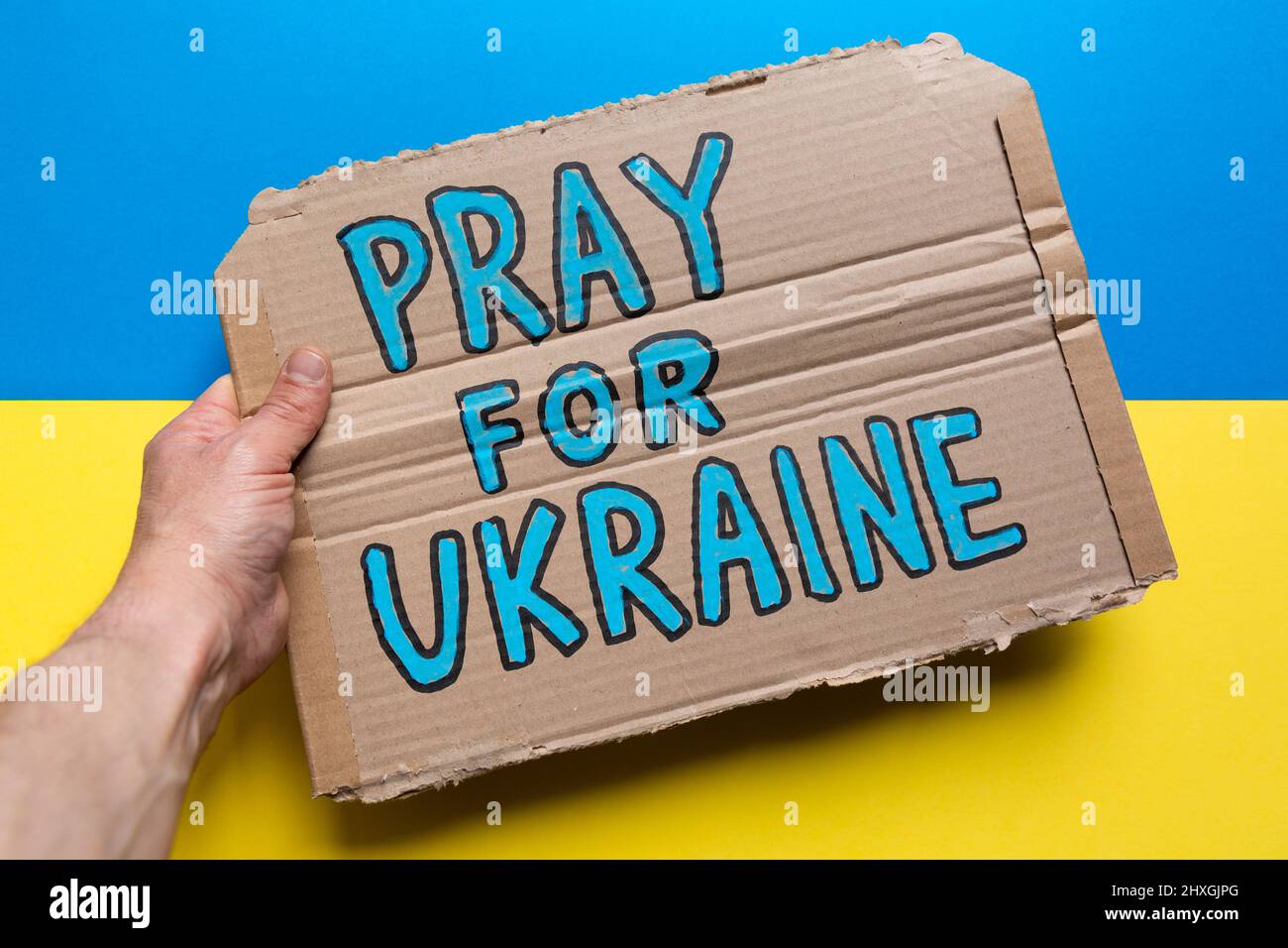 Mano umana che tiene un segno con la preghiera per lo slogan Ucraina sulla bandiera Ucraina. Foto Stock