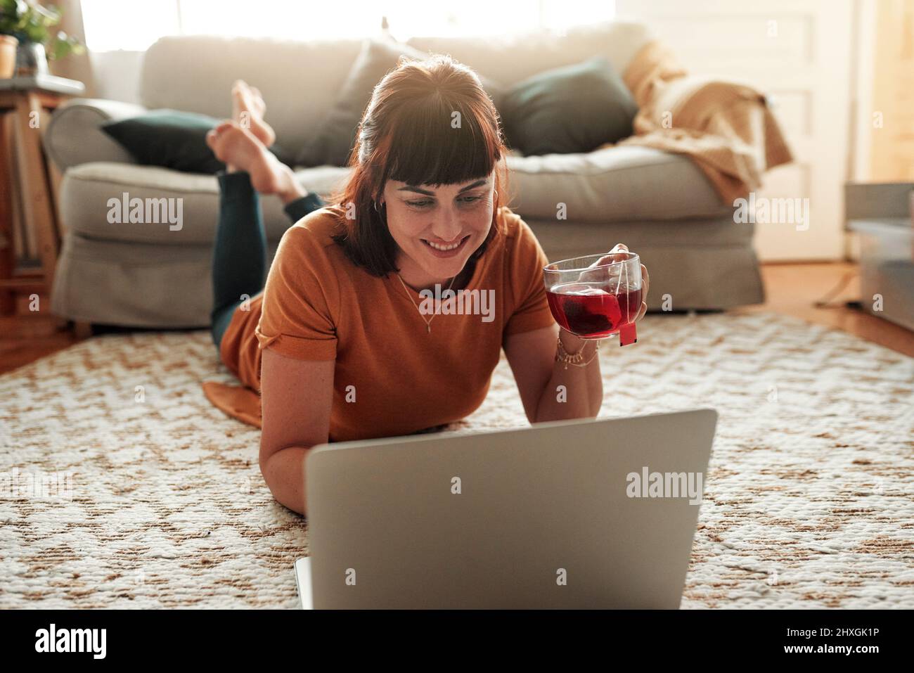 Prendi un po' di tè e preparati a divertirti. Scatto di una donna che usa il suo laptop mentre si rilassa a casa. Foto Stock