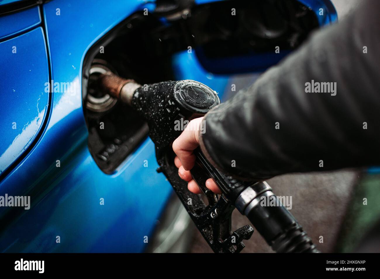 Uomo mano che tiene ugello carburante, il riempimento della sua auto. Clima freddo e piovoso Foto Stock