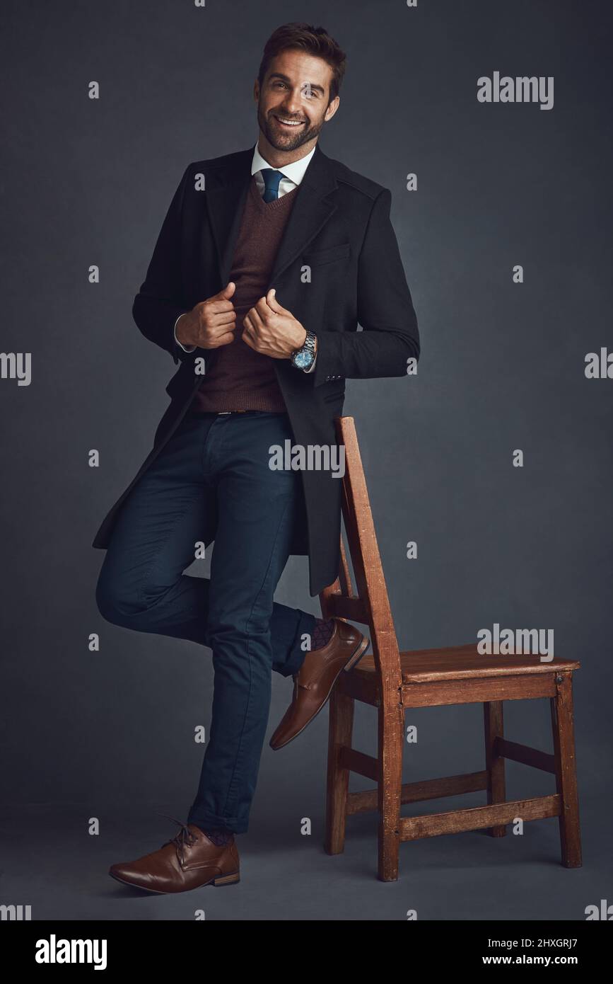 Permettetemi di essere la vostra ispirazione quotidiana. Ritratto di studio di un giovane uomo vestito con eleganza in piedi accanto ad una sedia su sfondo grigio. Foto Stock