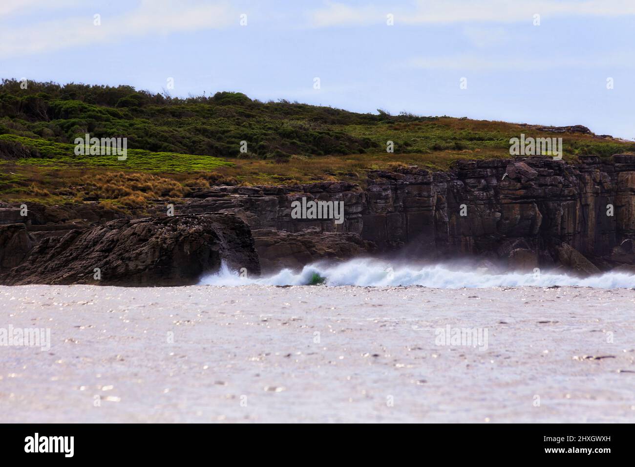Scogliere rocciose dell'isola di Bowen sulla costa pacifica della baia di Jervis dell'Australia ad alta marea e venti tempestosi che colpiscono le onde. Foto Stock
