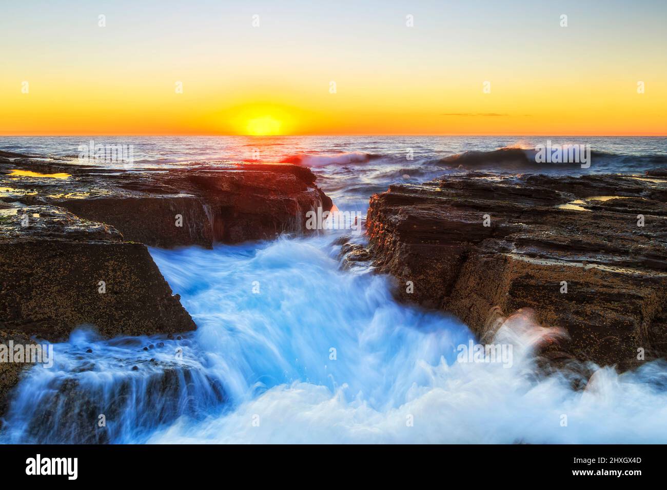 Narrabeen Beach arenaria rocce di un promontorio all'alba colpito dalle onde dell'oceano pacifico. Foto Stock