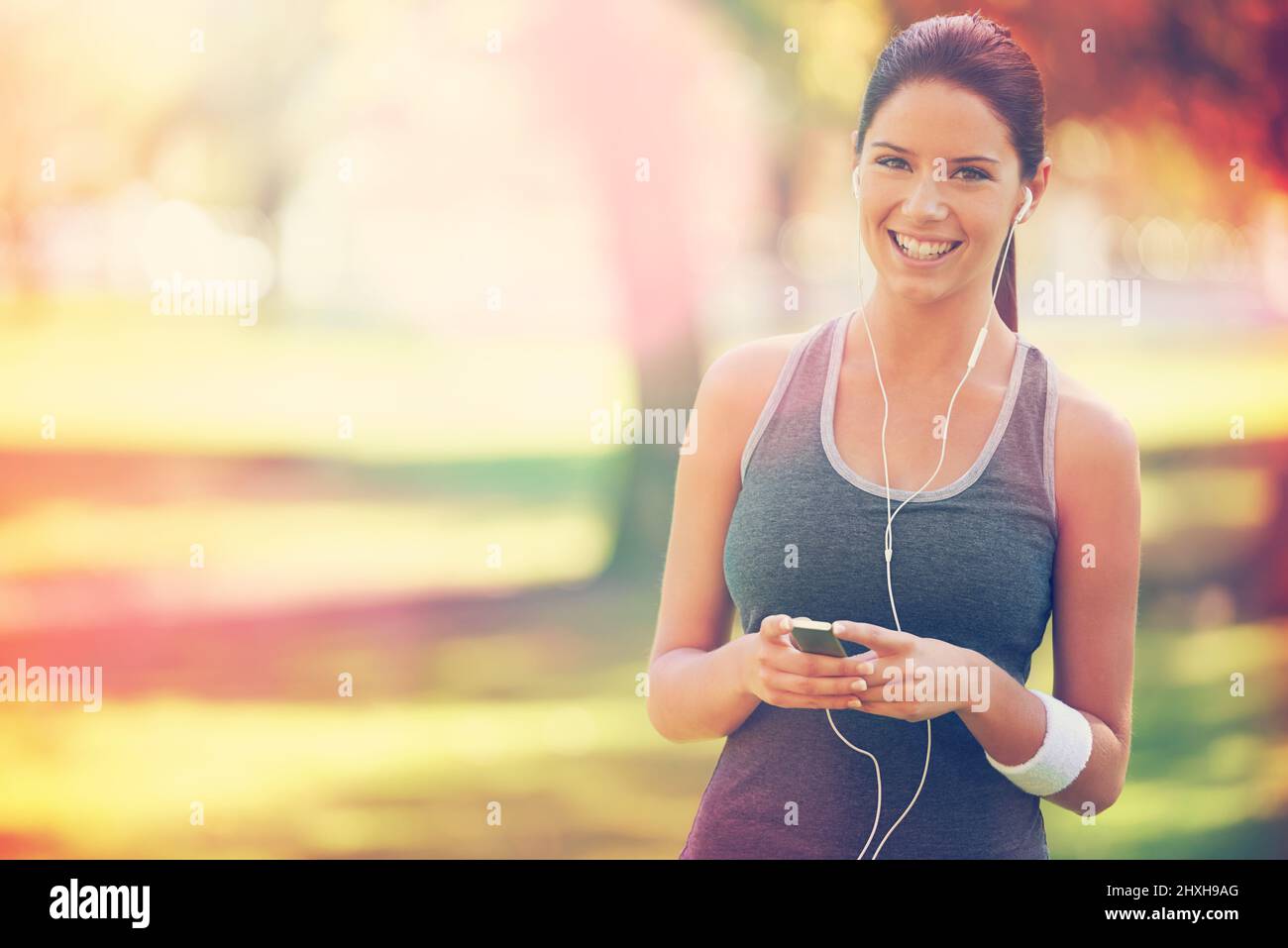 Playlist perfetta per una corsa nel parco. Scatto corto di un giovane corridore che indossa le cuffie. Foto Stock