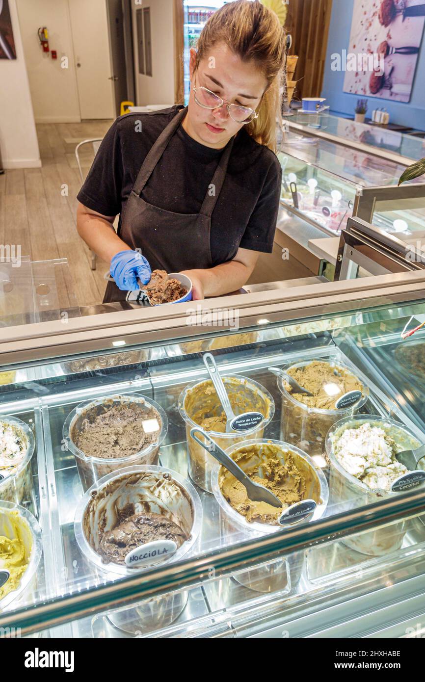 Miami Beach Florida Collins Avenue Inside Interior Freddo gelato negozio vetrina vendita caso ispanico donna staff dipendente preparazione tazza scooping Foto Stock