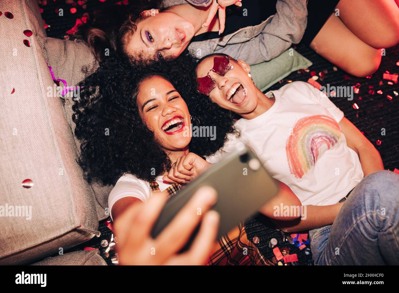 Selfie vibranti per persone vibranti. Vista dall'alto di tre amici felici che prendono un selfie mentre si trova sul pavimento ad una festa della casa. Gruppo di allegro Foto Stock