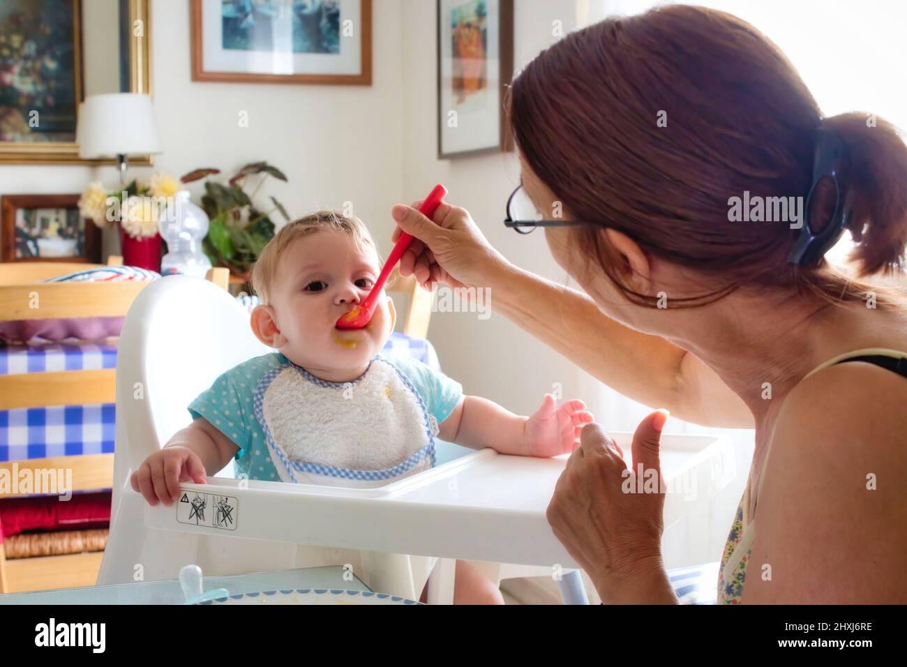 Bambino piccolo che è alimentato da sua nonna in un high-chair di plastica Foto Stock