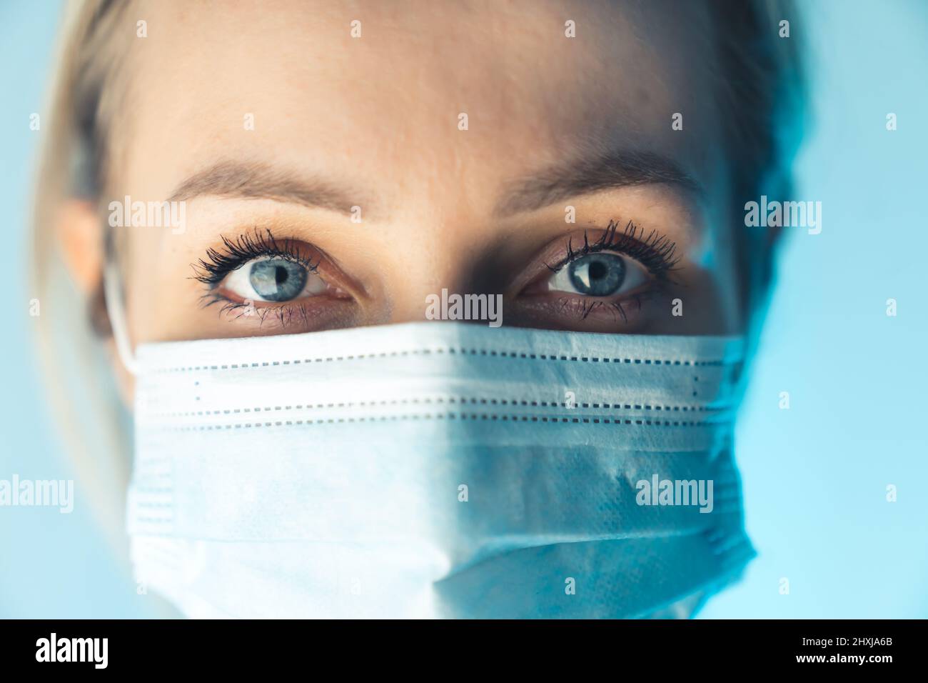 Primo piano ritratto di bella 30s giovane donna millenaria che copre il suo viso con maschera medica facciale blu. Foto studio. Foto di alta qualità Foto Stock