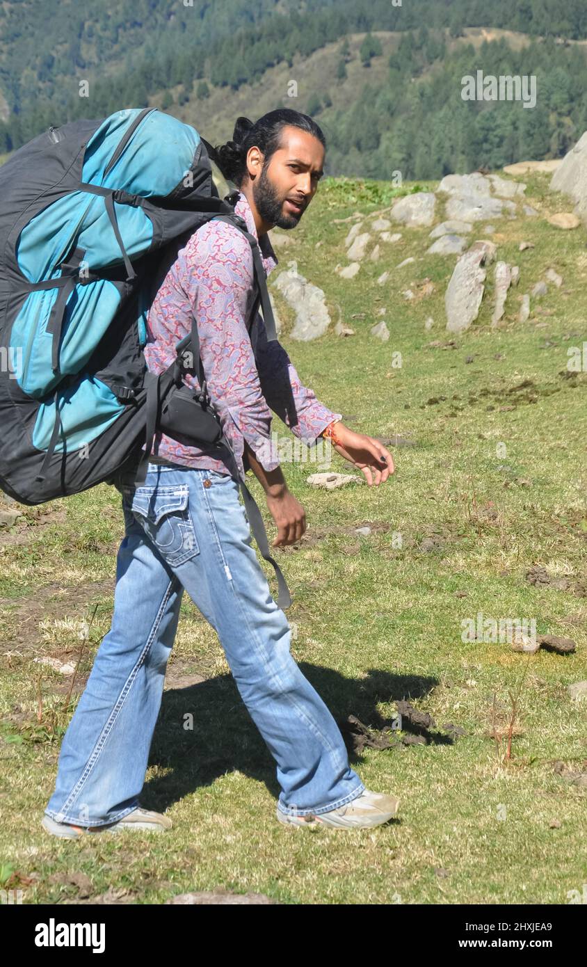 Vista laterale di un viaggiatore maschio che guarda la macchina fotografica mentre cammina sulla montagna con trasporto zaino paracadute Foto Stock