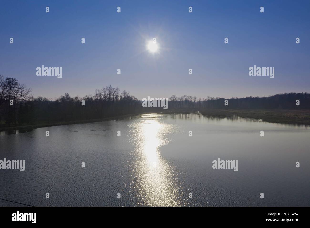 Un lago, un serbatoio d'acqua situato tra le foreste. Le rive sono ricoperte di canne gialle e secche. La luce del sole si riflette nell'acqua. Foto Stock