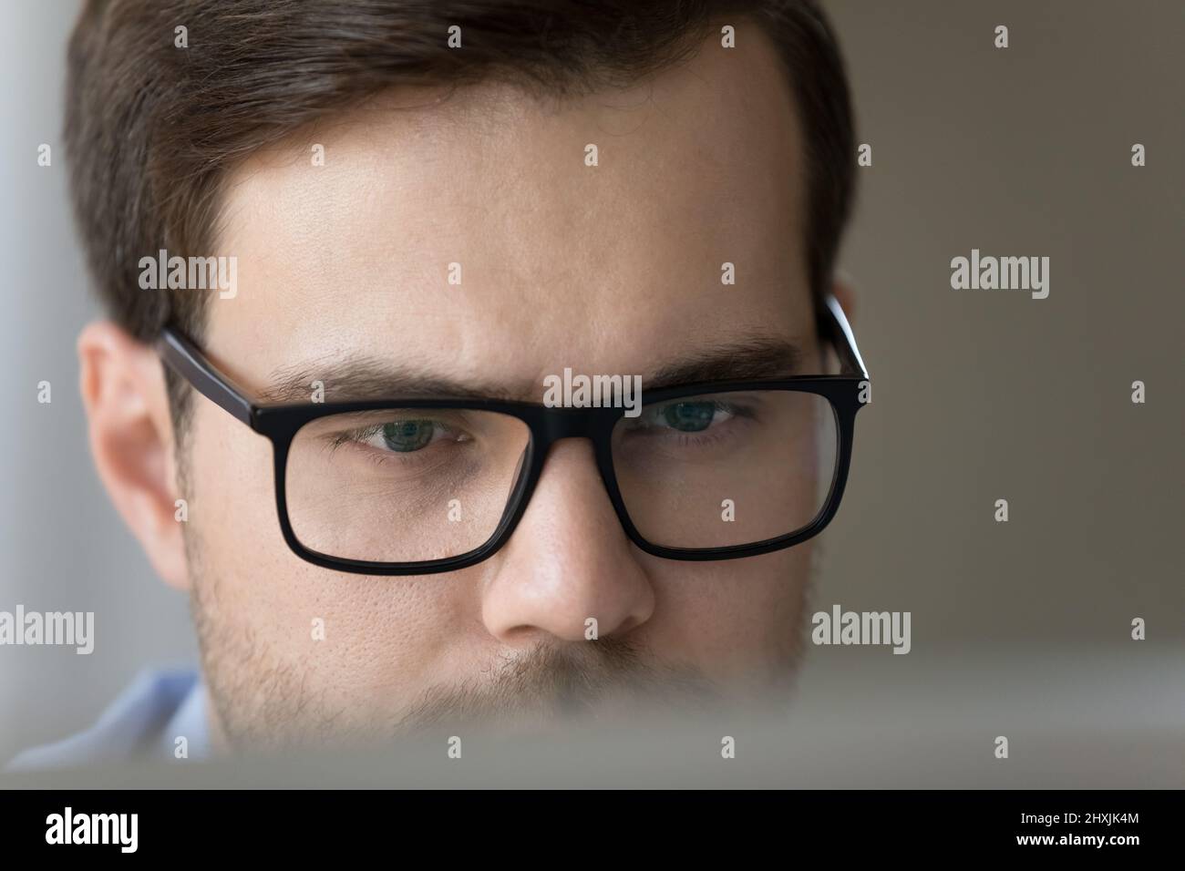 Primo piano concentrato maschio millenario in occhiali guardare sullo schermo del computer Foto Stock