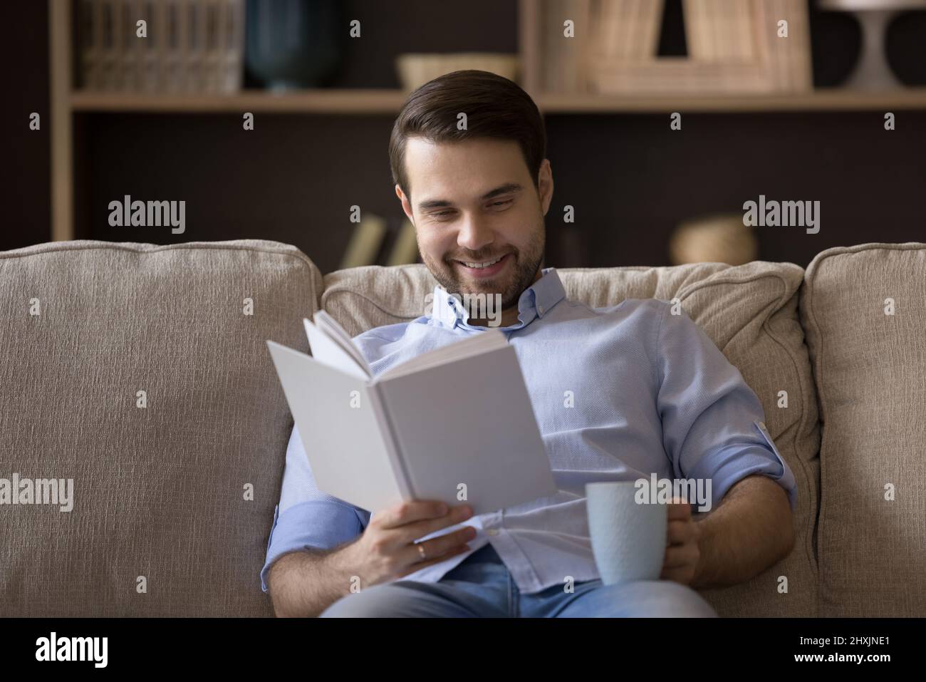Giovane uomo lettore che tiene una tazza di caffè godendo il libro preferito Foto Stock