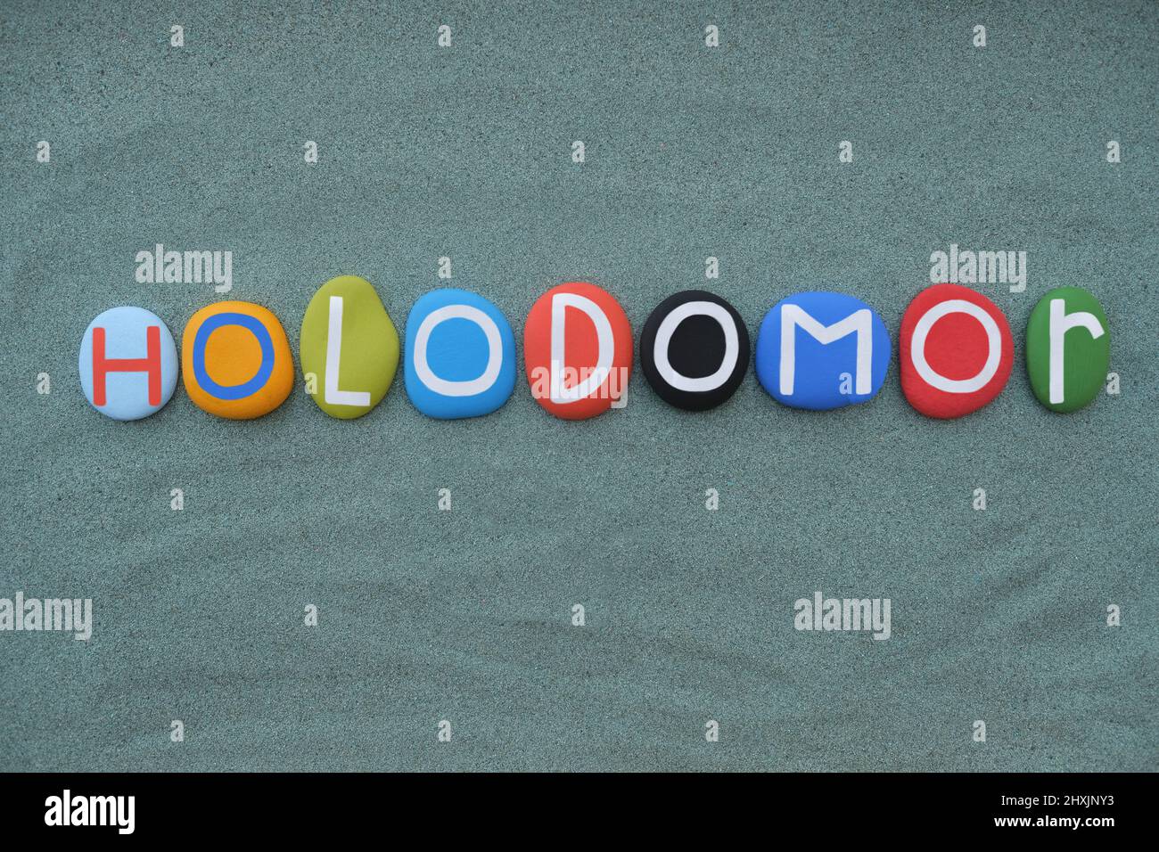 Holodomor, morte per fame, in ucraino, testo di lettere in pietra multicolore composto su sabbia verde Foto Stock