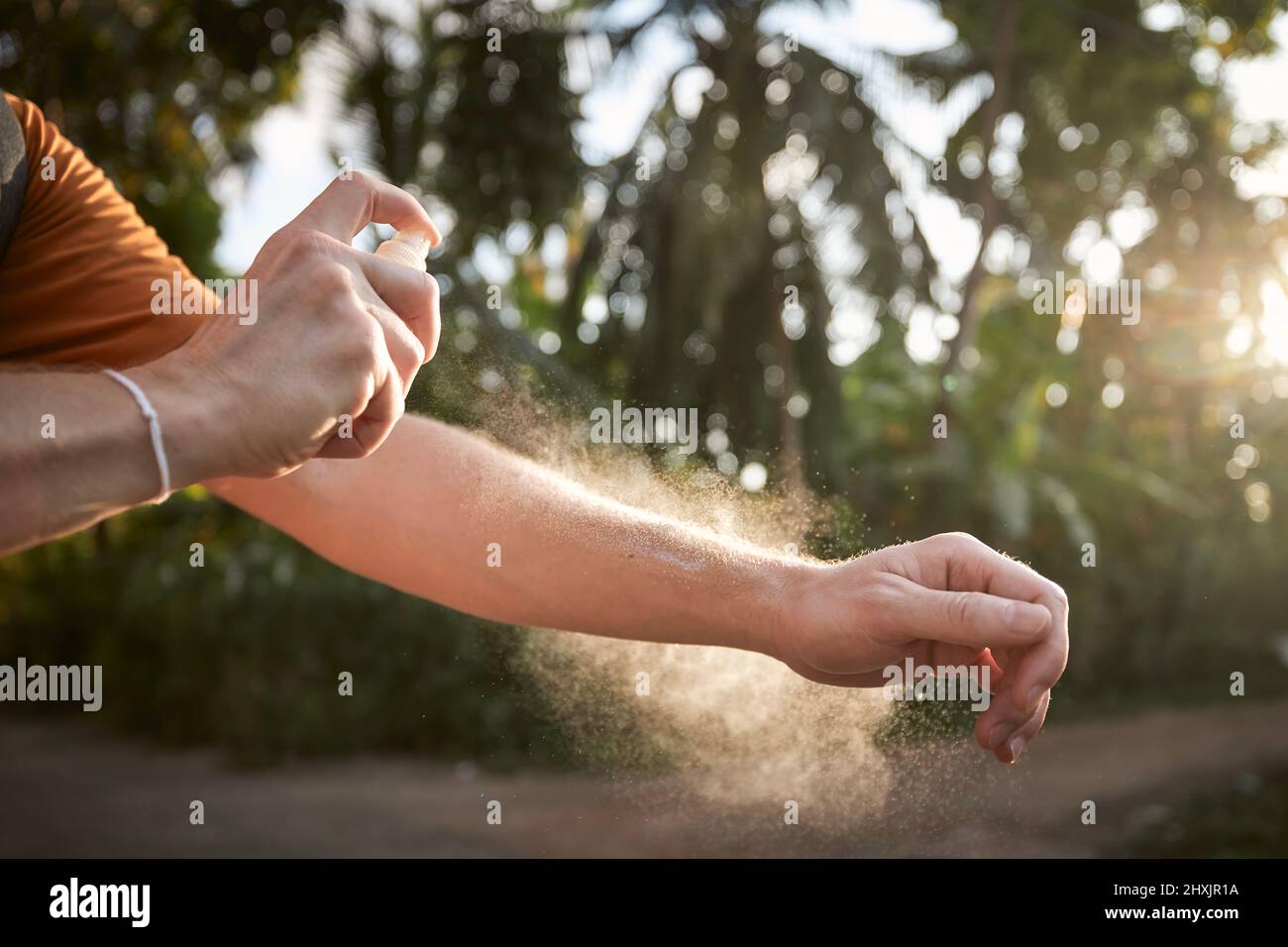 Prevenzione contro morso di zanzara in destinazione tropicale. Uomo che applica repellente per insetti sulla sua mano contro le palme. Foto Stock