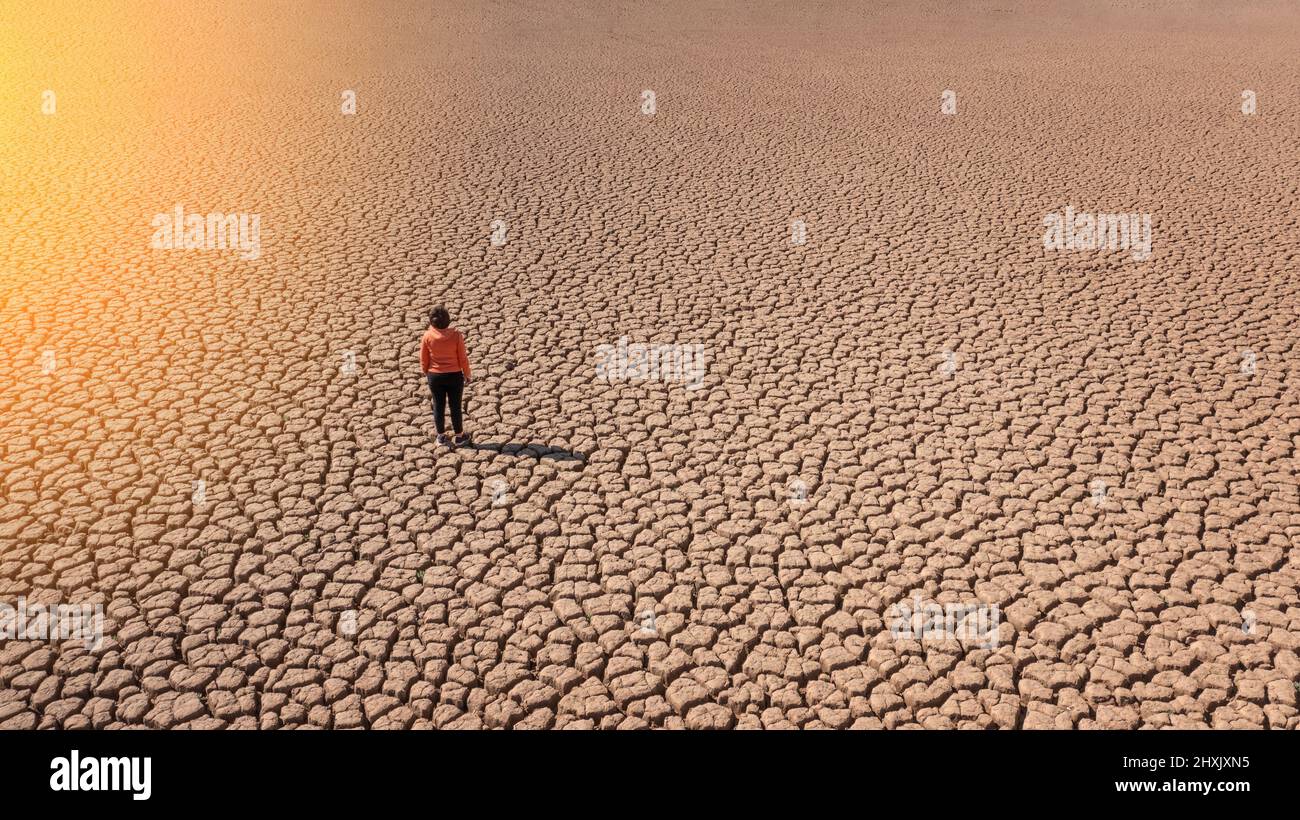 Silhouette di un uomo su una terra sabbiosa spaccata vuota e non fertile durante una siccità. Il concetto di catastrofe ecologica sul pianeta. Giorno di sole Foto Stock