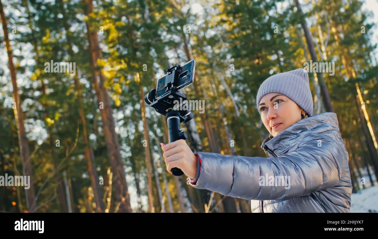 Donna che tiene su pellicola portatile 3-asse dispositivo di stabilizzazione gimbal in inverno per smartphone. Ragazza Blogger rendere Selfie, Broadcast Video Blogging, Vlogging. Operatore di videografo scatta foto video. Foto Stock