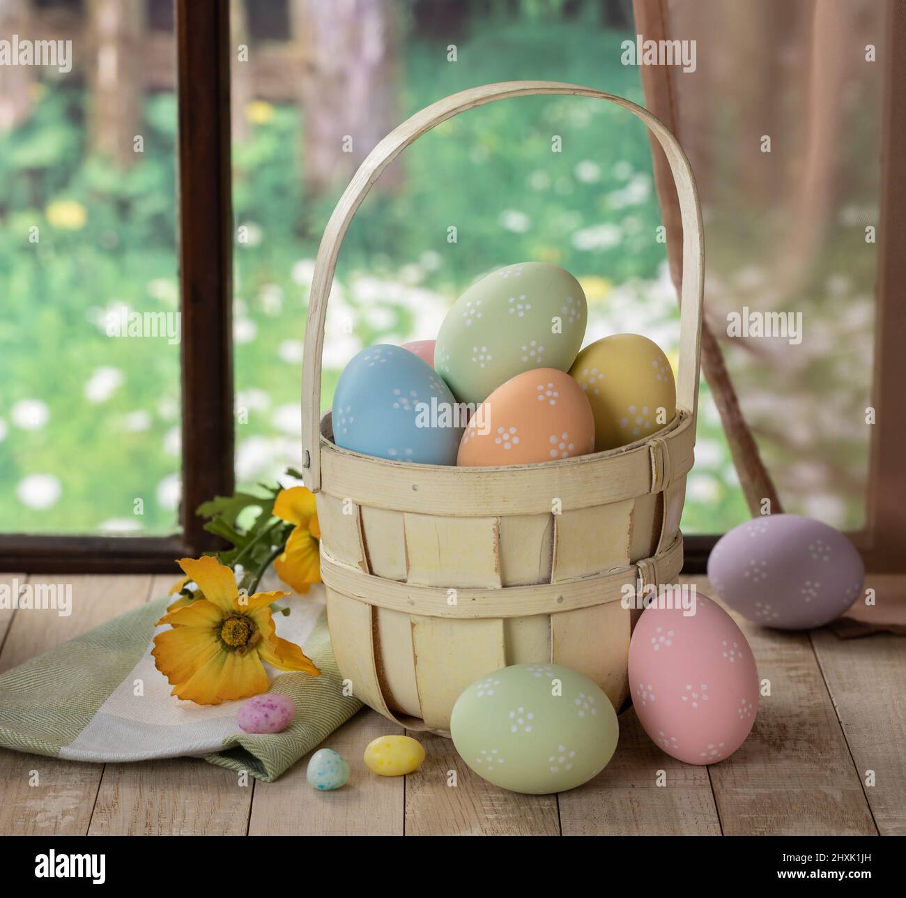 Uova di pasqua colorate in un cestino e su un tavolo di legno da una finestra con sfondo rurale Foto Stock