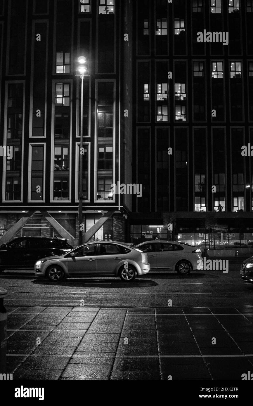 Ritratto girato del Strand, Liverpool, con traffico assortito, trascurato da grattacieli torreggianti in bianco e nero. Foto Stock
