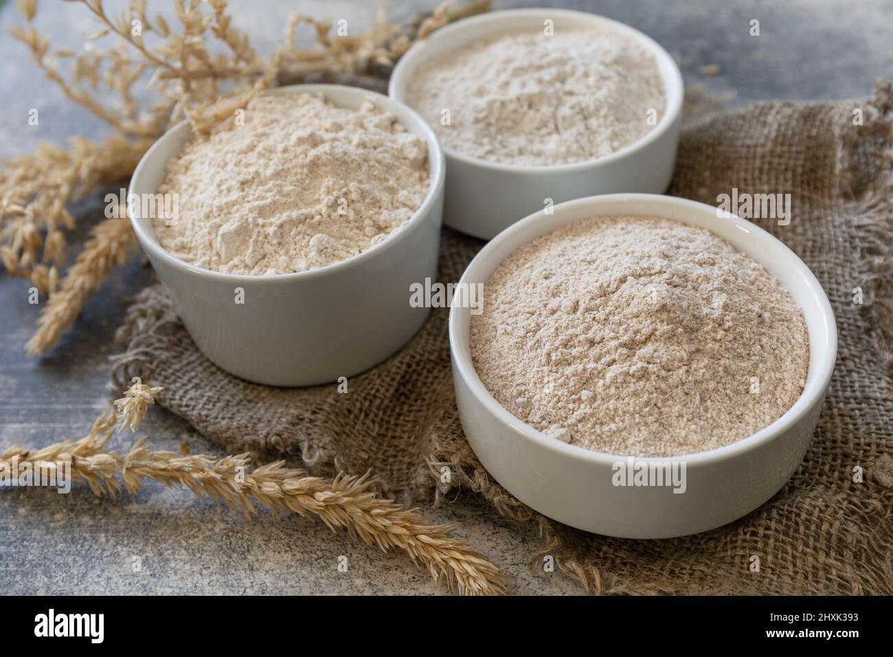 Cibo e ingredienti di cottura. Farina di frumento a grana grossa da grani interi, crusca di frumento e farina di frumento su fondo di pietra grigia. Foto Stock