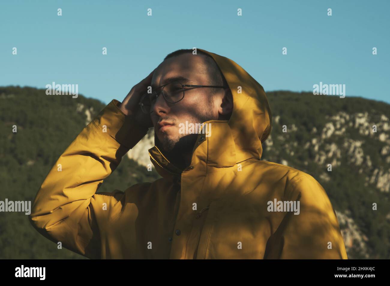 Ritratto di un uomo 20s con vetri e mantello giallo in montagna. Foto Stock