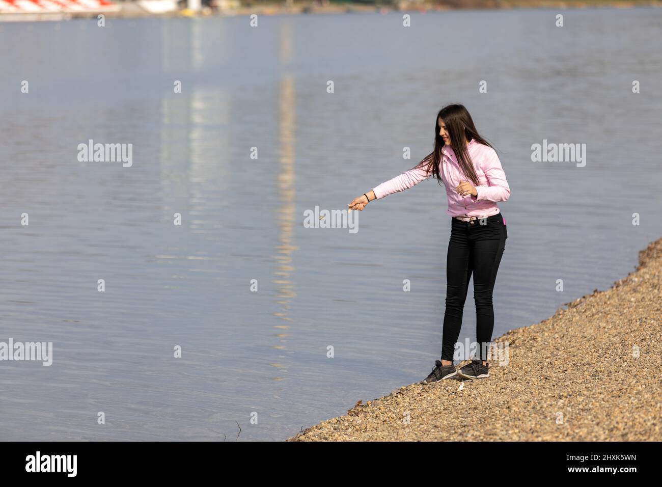 Una giovane ragazza in piedi sulla riva del lago e gettare pietre in acqua. Ricreazione in natura, tempo libero, passeggiate all'aria aperta. Foto Stock