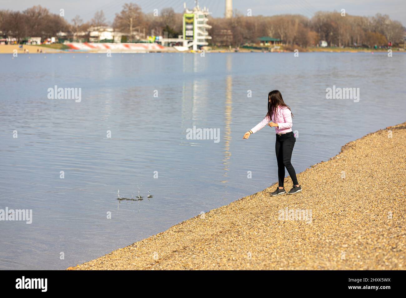 Una giovane ragazza in piedi sulla riva del lago e gettare pietre in acqua. Ricreazione in natura, tempo libero, passeggiate all'aria aperta. Foto Stock