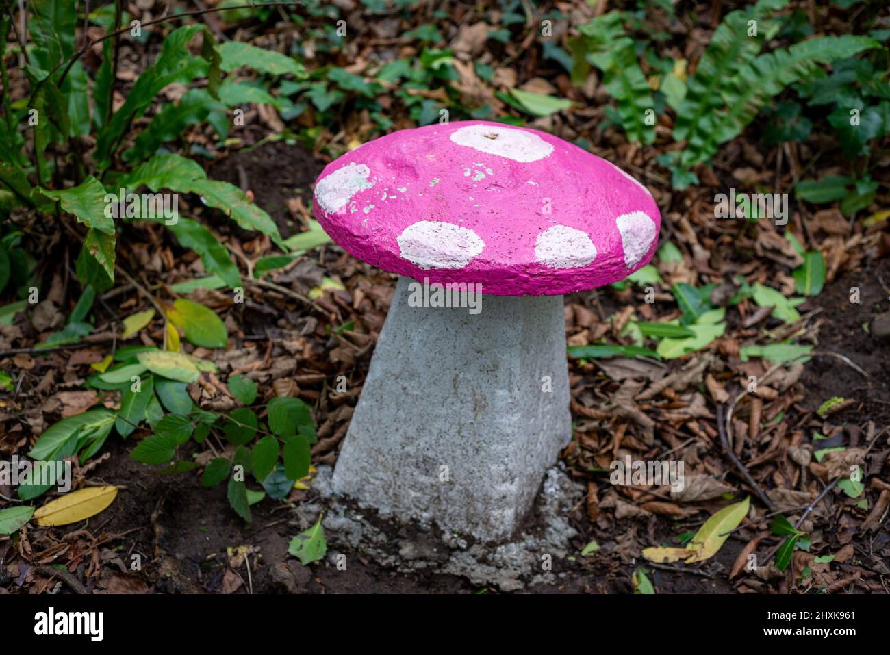 Sedile a fungo in pietra dipinto di rosa e bianco nel giardino delle fate incantato nei boschi. Foto Stock