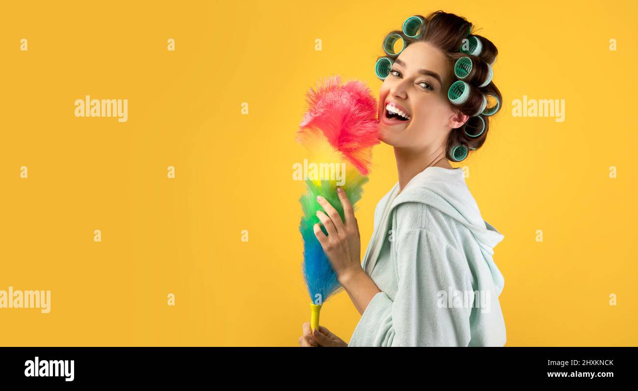 Donna felice con arricciacapelli che tiene Duster Feather, sfondo giallo Foto Stock