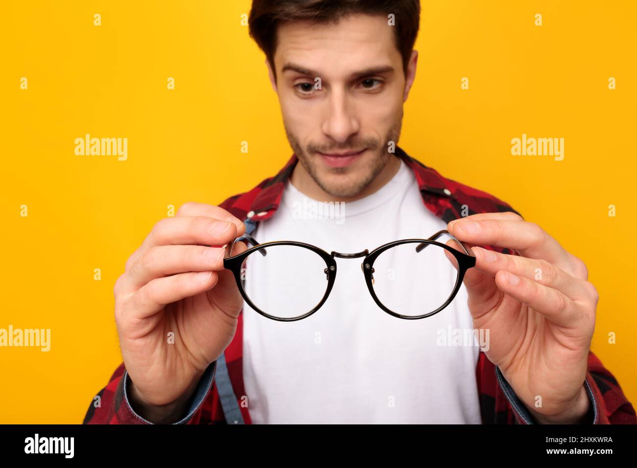 Primo piano del giovane uomo che tiene e guarda gli occhiali Foto Stock