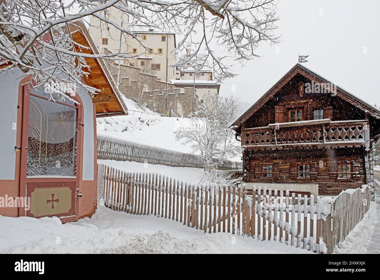 Piccola vecchia casa di legno con recinzione in legno e cappella in primo piano, Fortressin sfondo tutto coperto di neve, Mauterndorf, Austria Foto Stock