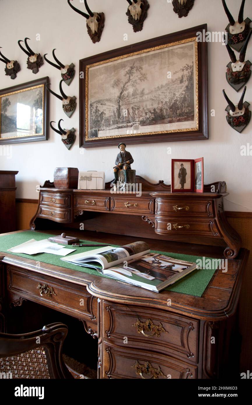 scrivania intagliata con cassetti, libro e lettere davanti al muro con incisioni e trofei di camoscio Foto Stock