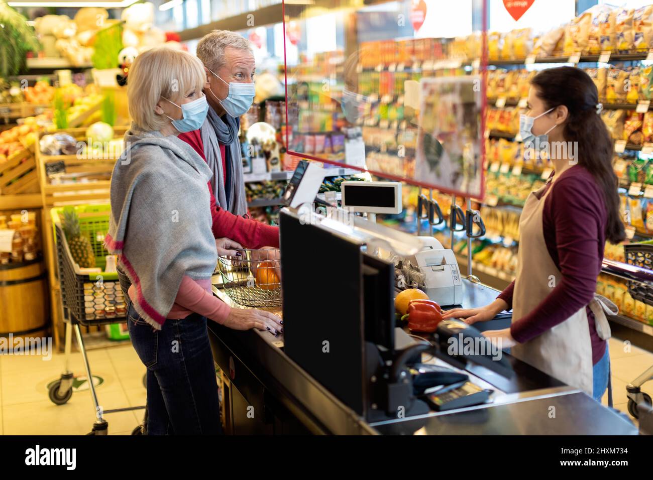 Coppia anziana in maschere facciali paganti al banco cassa al supermercato Foto Stock