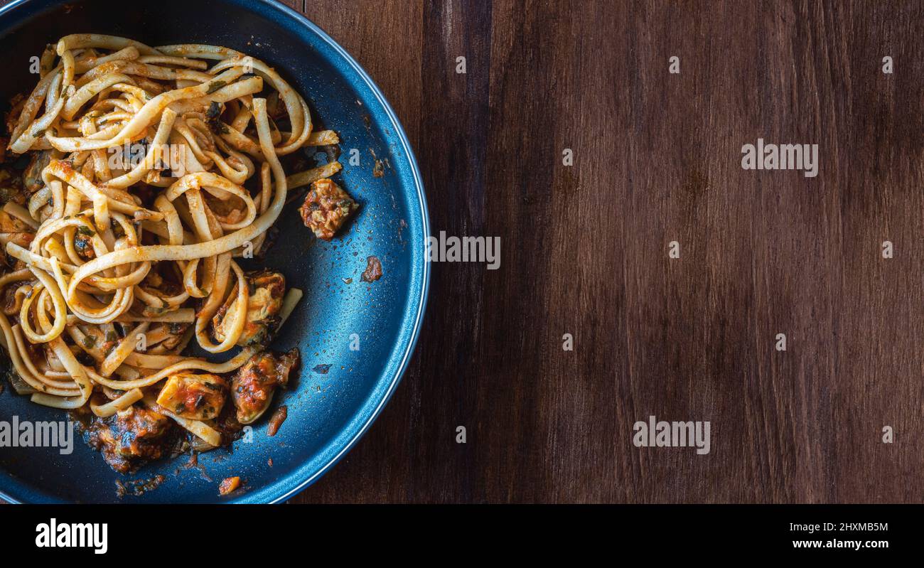 Padella di spaghetti con cozze, pesce e salsa di pomodoro appena sfornata. Fatto in casa. Su tavola di legno, vista dall'alto. Ambiente piatto. Orizzontale. Foto Stock