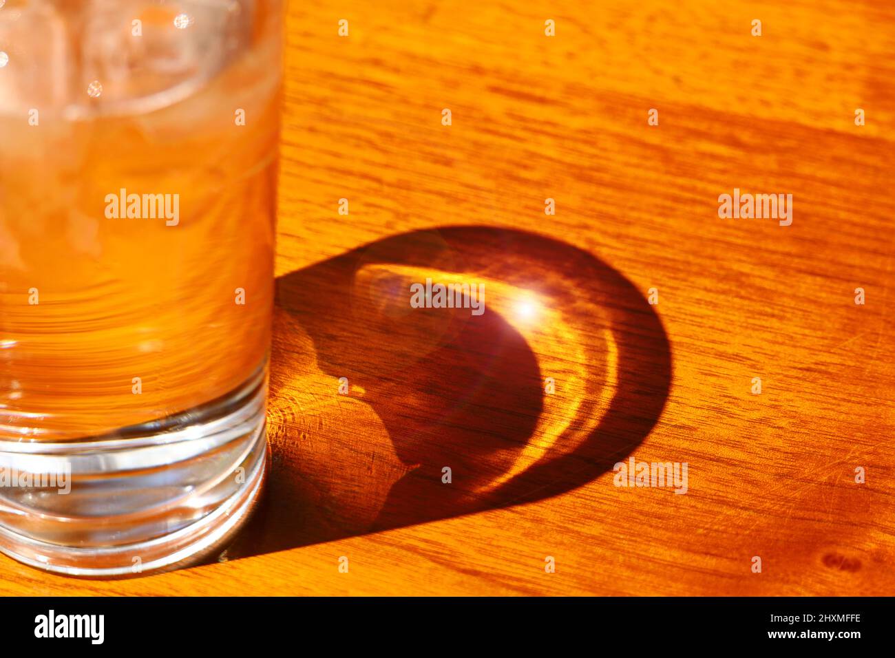 Luce e ombra sul tavolo dove il sole splende attraverso un bicchiere freddo di ghiaccio e acqua Foto Stock