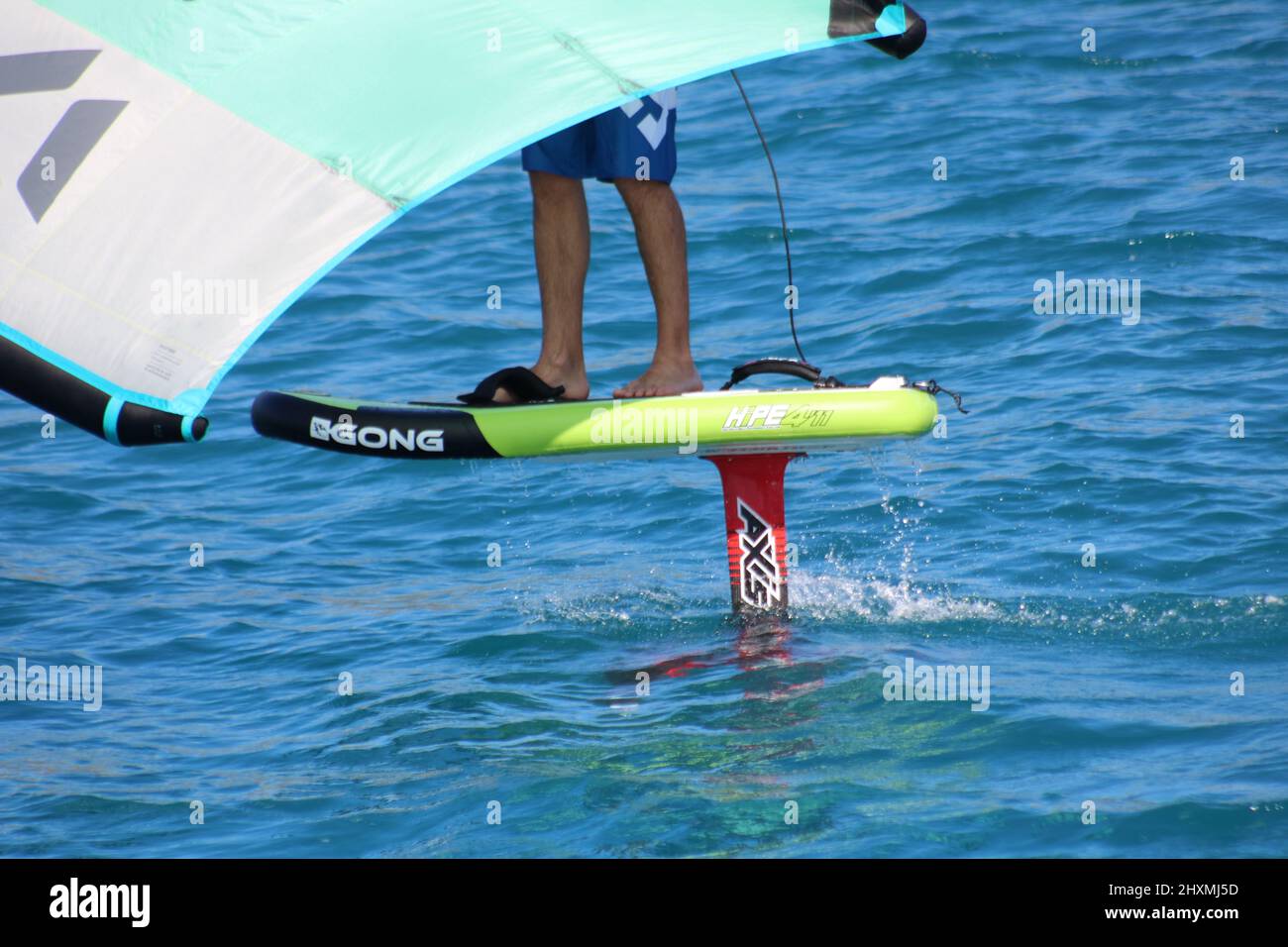 Primo piano delle gambe di un uomo vento foil surf su una tavola Gong con la pinna bene fuori dall'acqua Foto Stock