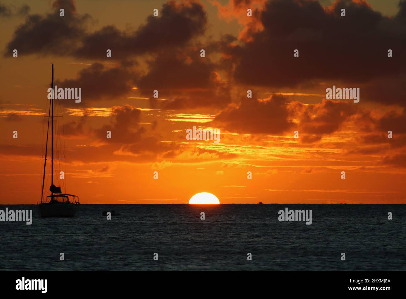 Perfetto mezzo sole che scende nei Caraibi con uno yacht in primo piano e un po' di dettagli nuvolosa Foto Stock