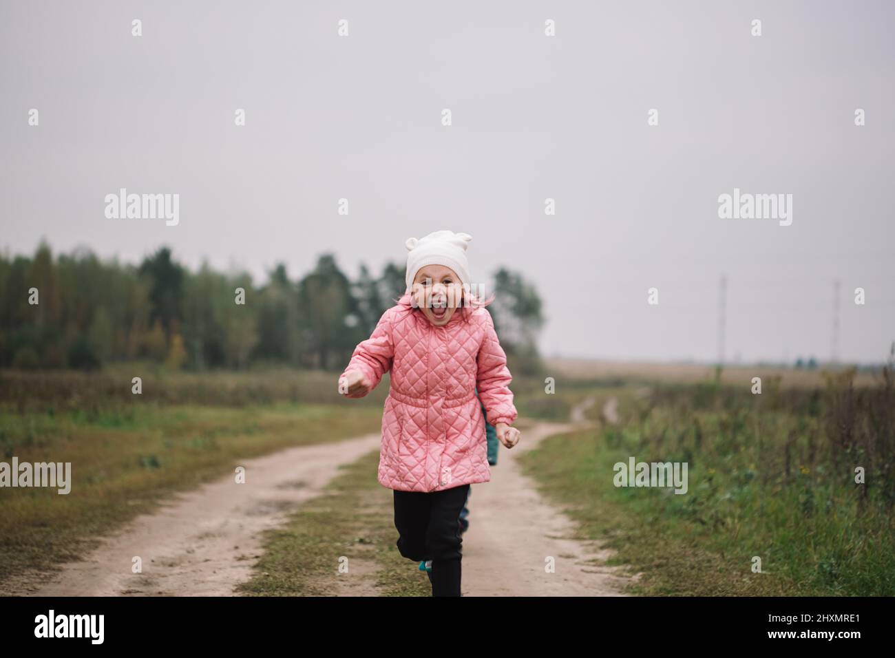 Piccola ragazza caucasica che corre in campo con suo fratello fare volti divertenti. Foto Stock