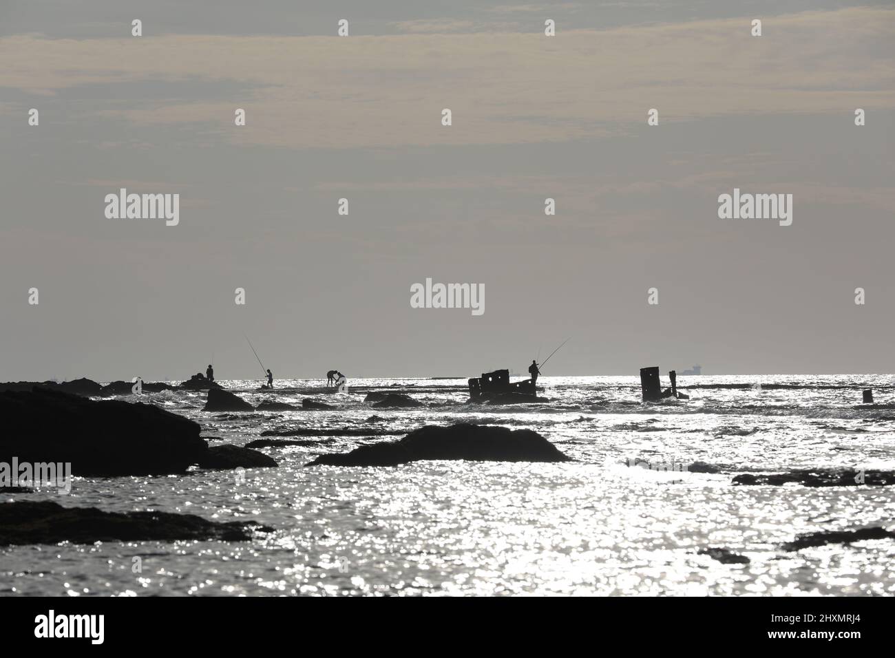 Vista lungo la costa che mostra mensole di pietra di sabbia lavica e piscine di acqua di mare. Il cielo è blu come le onde di marea si infrangono su rocce sommerse dentro Foto Stock