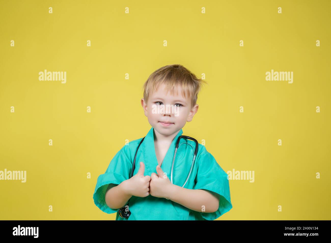 Ritratto di carino ragazzo caucasico vestito di medici verde mostrando pollice su gesto su sfondo giallo Foto Stock