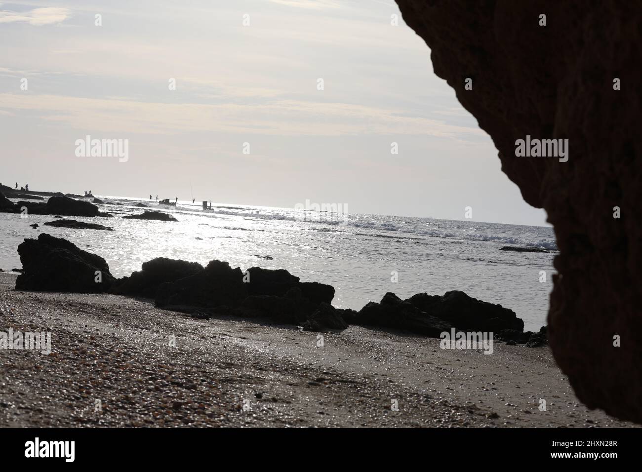 Vista lungo la costa che mostra mensole di pietra di sabbia lavica e piscine di acqua di mare. Il cielo è blu come le onde di marea si infrangono su rocce sommerse dentro Foto Stock