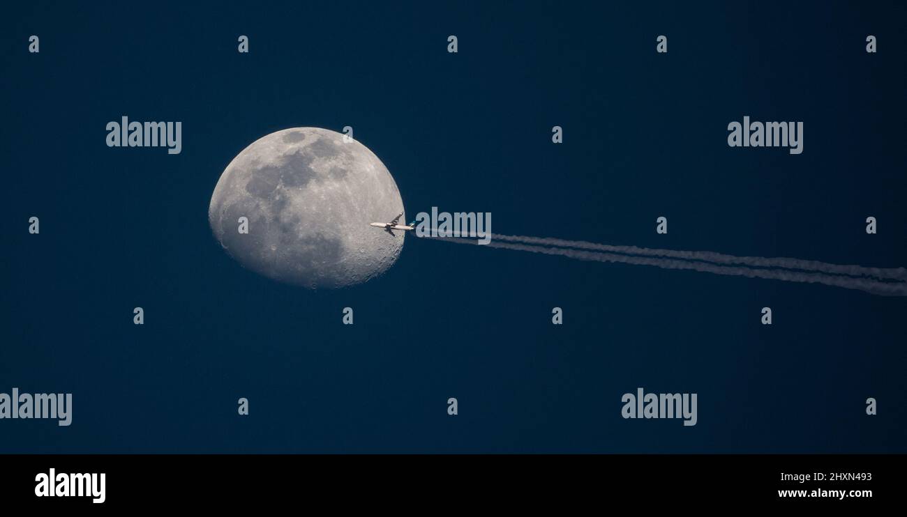 Un aereo di linea commerciale ad alta quota passa di fronte alla luna al tramonto. Foto Stock