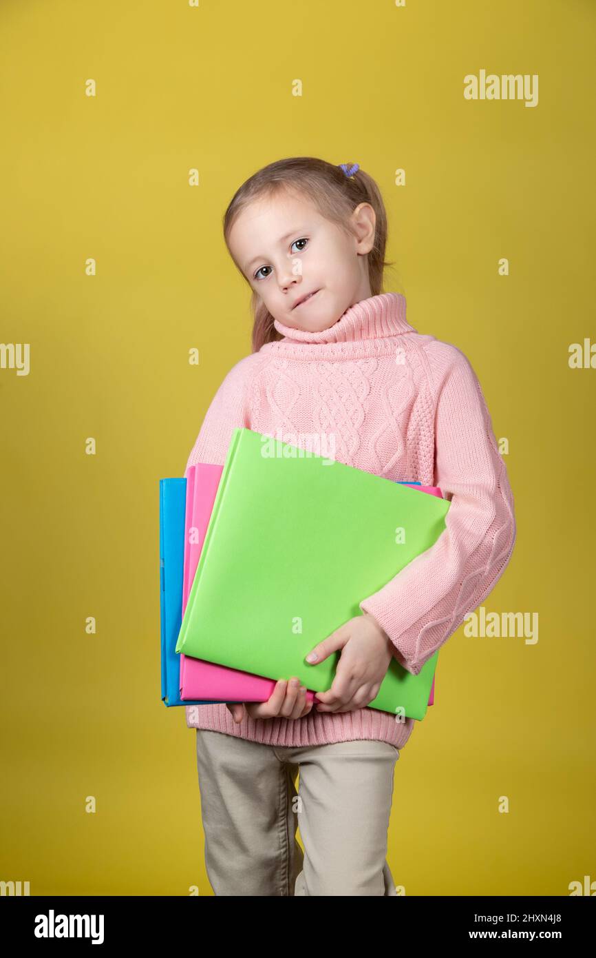 Ritratto di attraente ragazza della scuola di età elementare su sfondo giallo tenendo libri Foto Stock