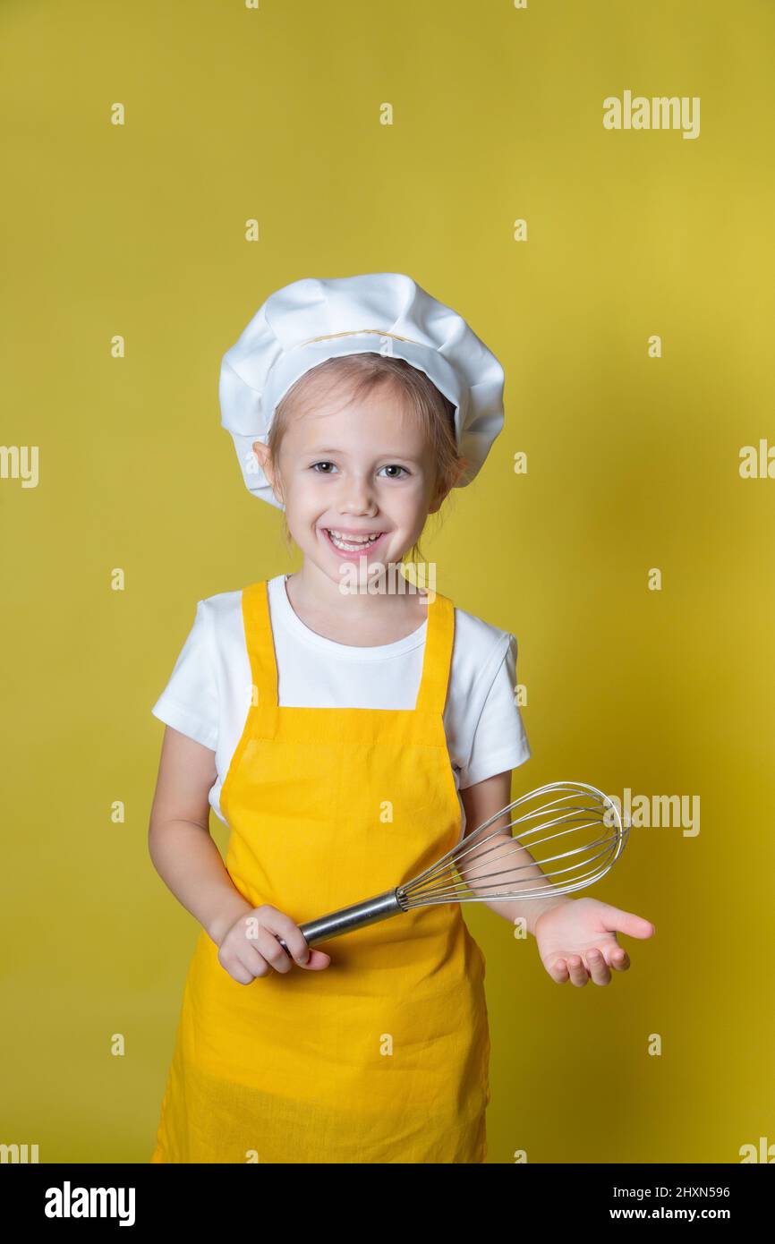 Ragazza in grembiule e cappello dello chef con un frusta per montare la panna Foto Stock