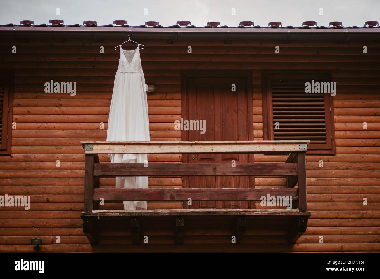 Abito da sposa lungo bianco appeso su un appendiabiti sul balcone di cottage in legno. Stile elegante e moderno. Design elegante. Stile estivo. Foto Stock