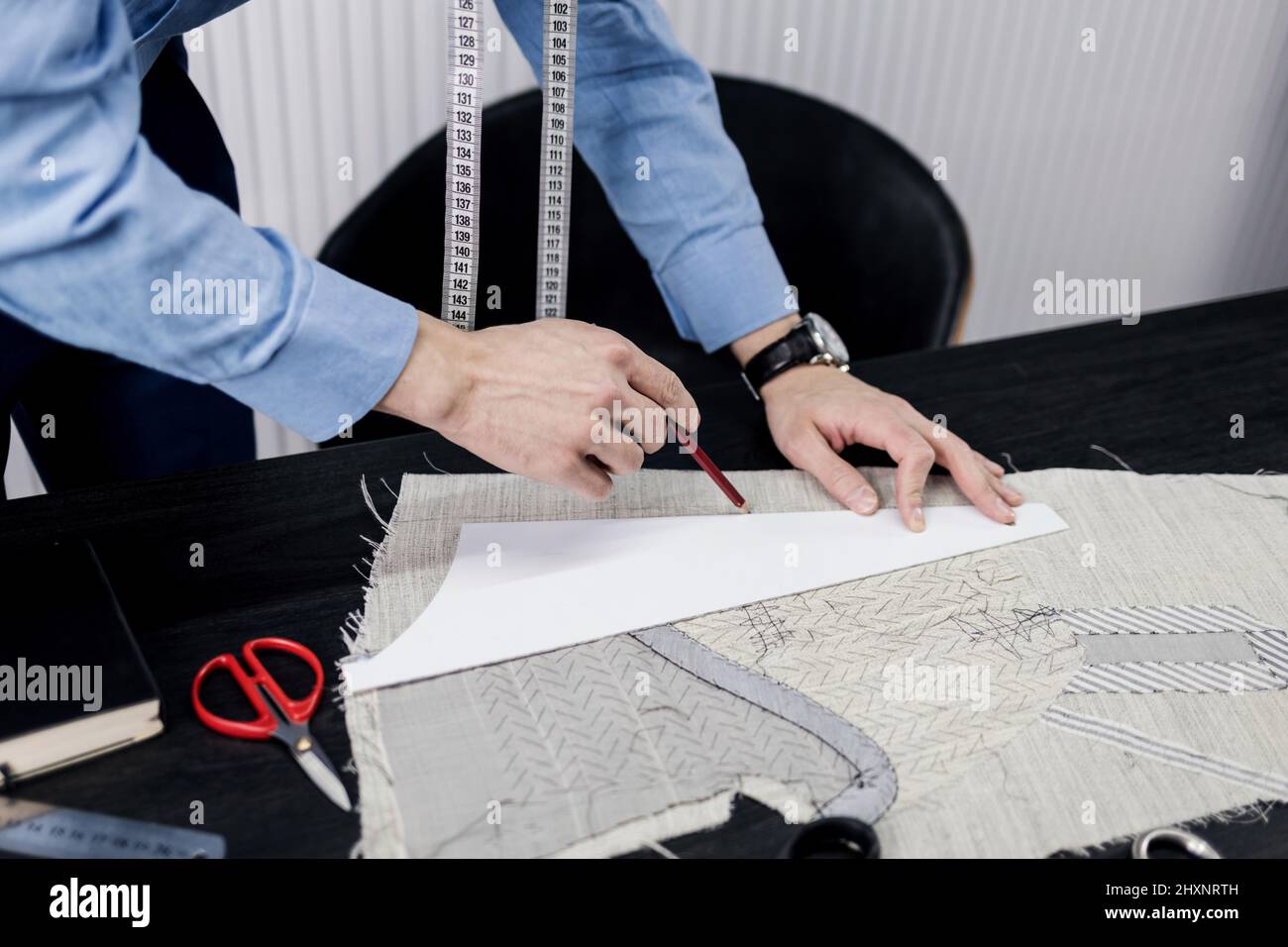 L'uomo su misura che lavora nel suo negozio su misura. Il maestro di sartoria in officina delinea le linee di taglio Foto Stock