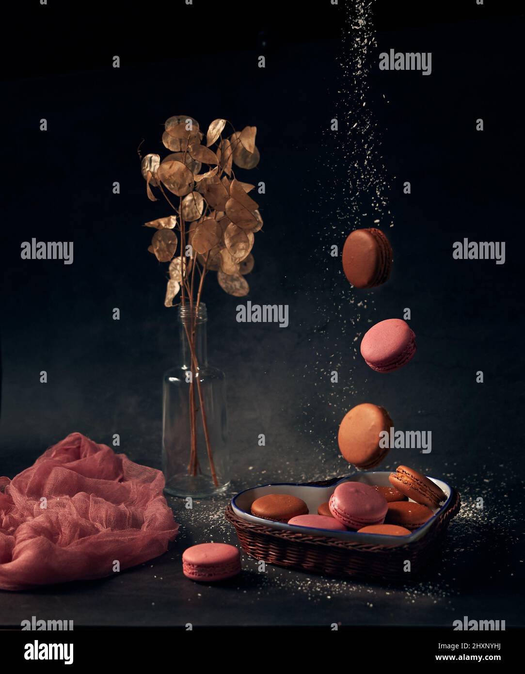 Le torte di fusione multicolore cadono in un vaso di paglia a forma di cuore con un bouquet di fiori secchi su sfondo nero Foto Stock