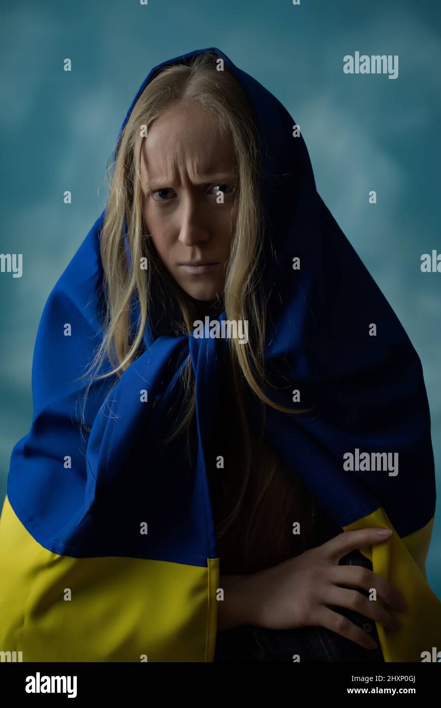 Una vera donna bionda Ucraina è sconvolta dal male e delusa durante la guerra con la bandiera Ucraina gialla e blu di stato sulla sua testa. La Russia ha attaccato l'Ucraina il 24 febbraio 2022. Foto Stock