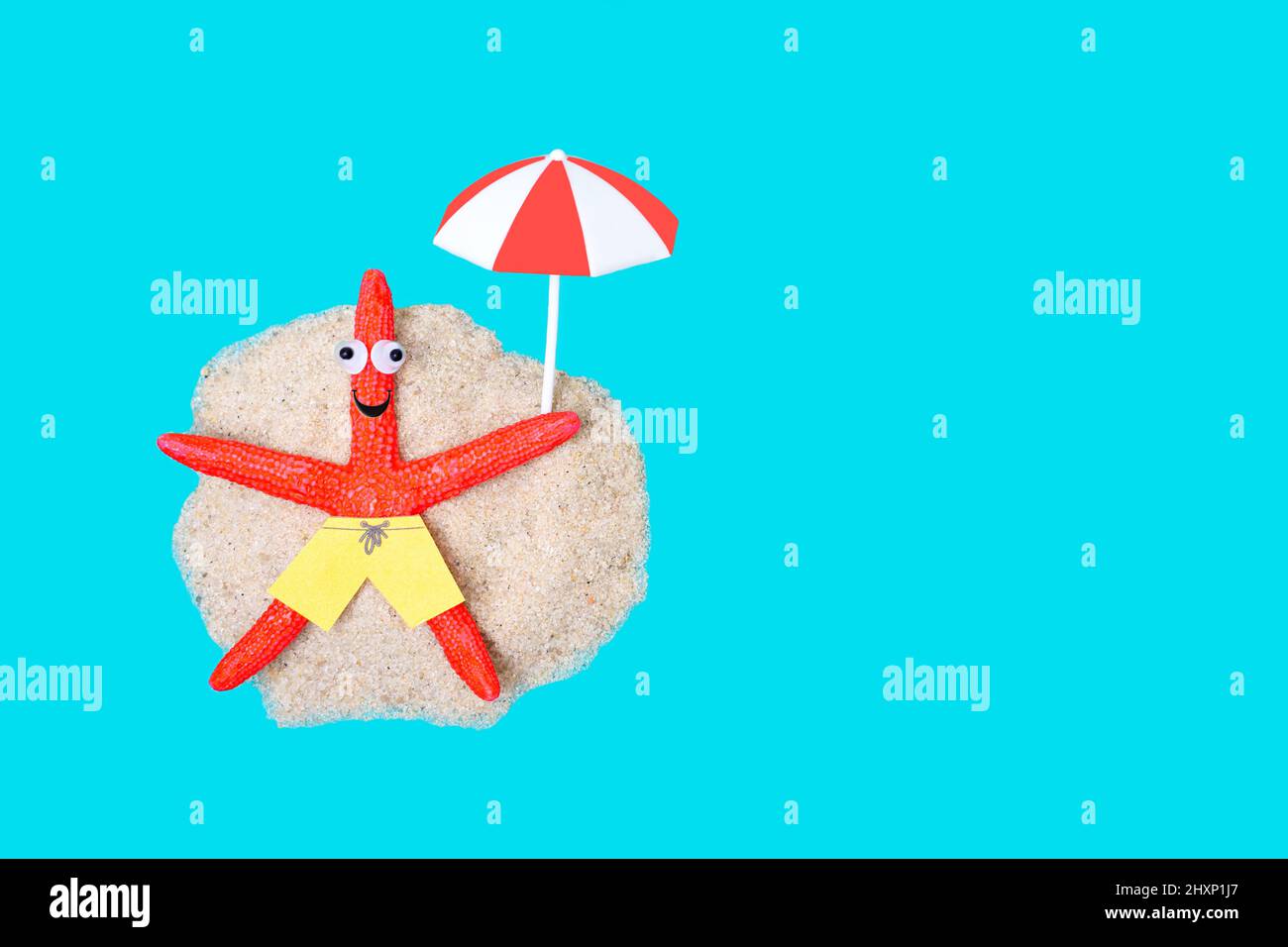 Carino carattere di stelle marine con occhi di googly che prendono il sole sotto un ombrellone su un'isola remota. Foto Stock