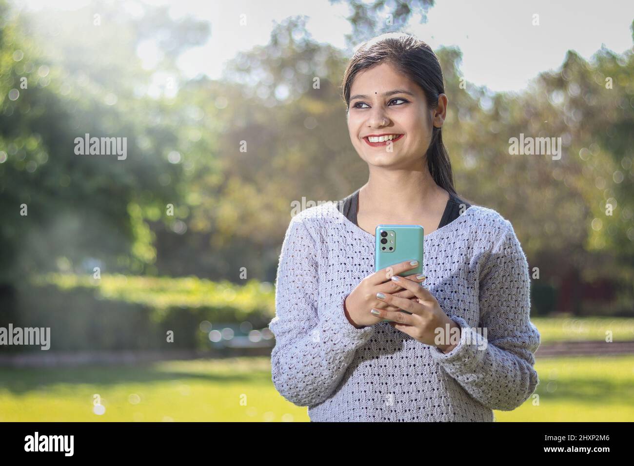 ritratto esterno di ragazza sorridente usando il telefono cellulare e guardando da parte. Foto Stock