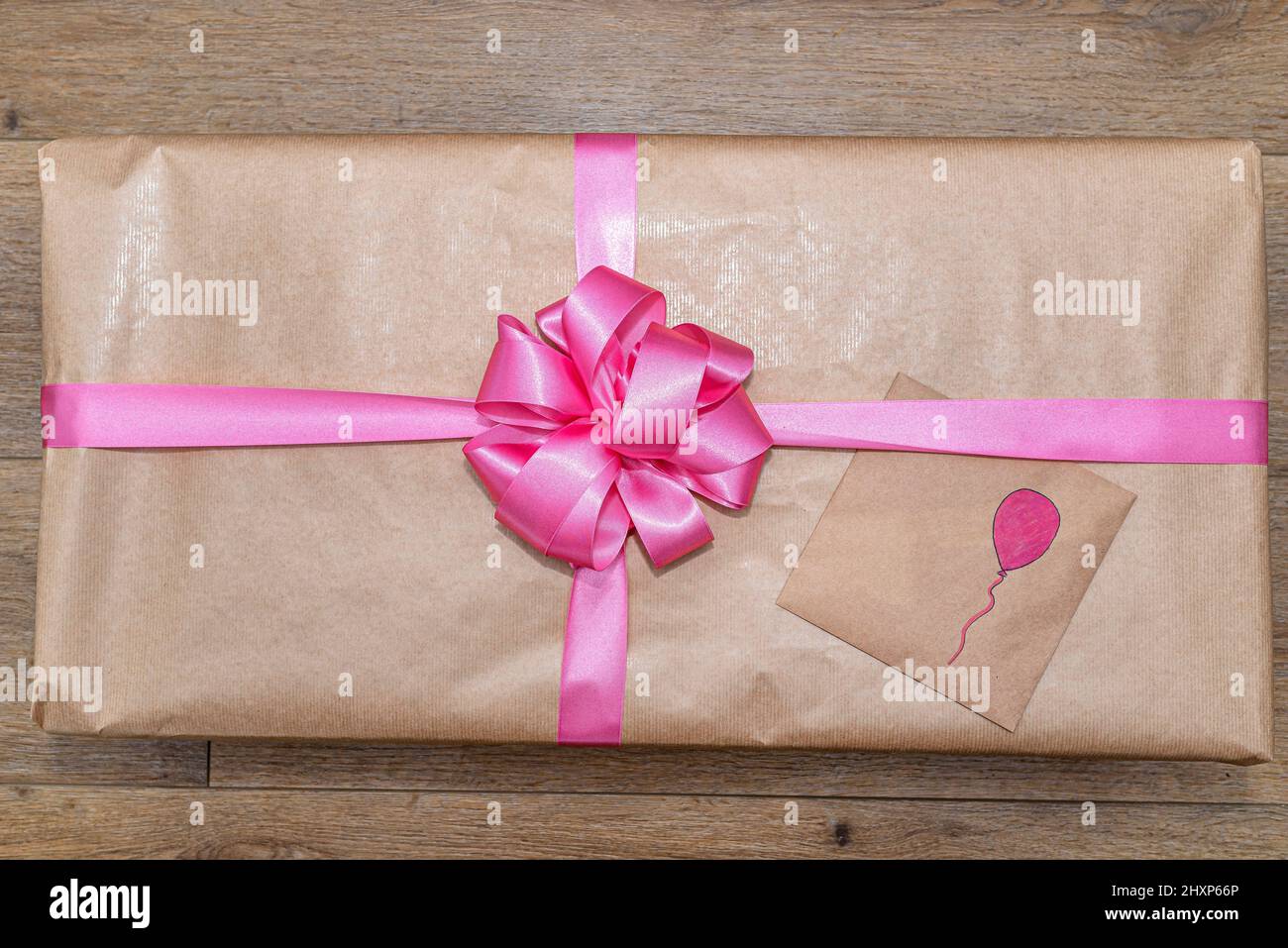 Un regalo avvolto in carta grigia avvolto con un nastro rosa legato ad arco, con un palloncino dipinto sulla busta. Foto Stock