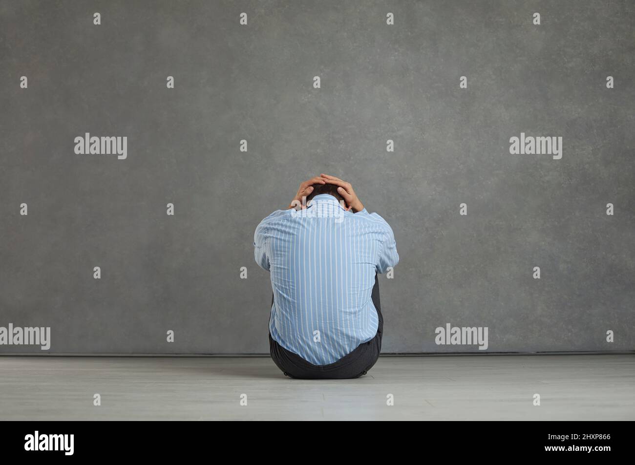 Vista posteriore dell'uomo seduto sul pavimento, che tiene la testa, che si sente angosciato, frustrato e senza speranza Foto Stock